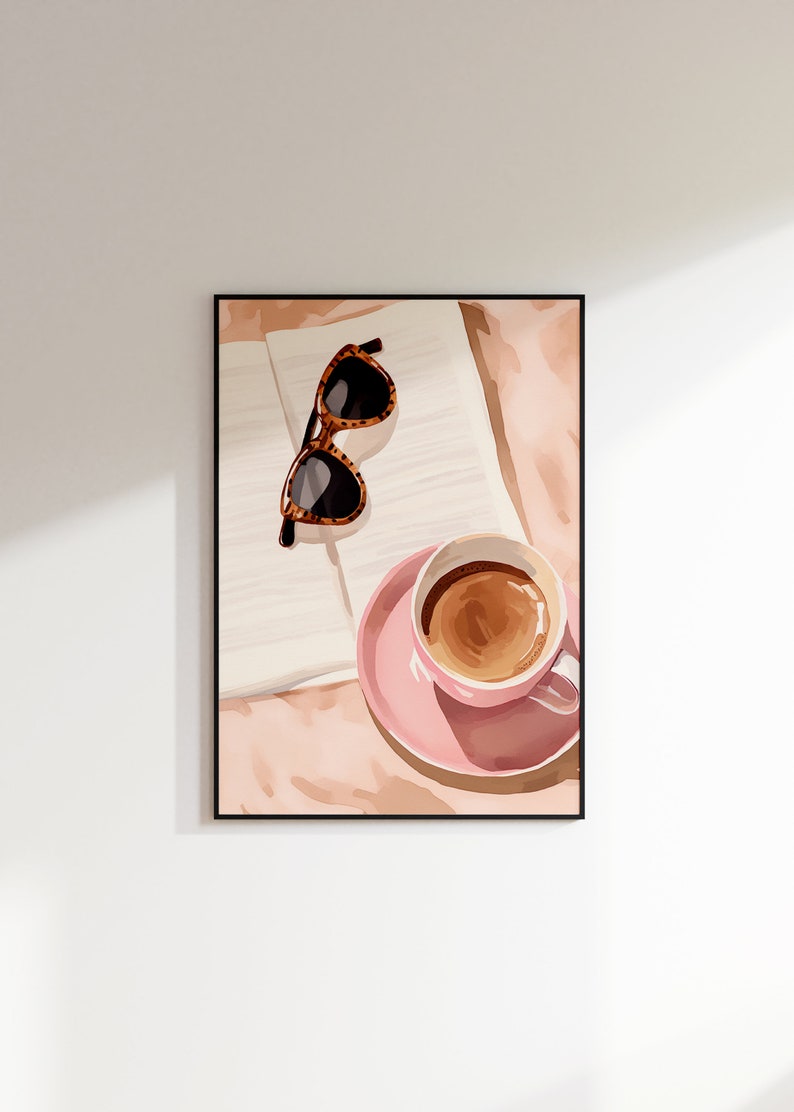 K&ouml;nnte beinhalten: Eine rosa Kaffeetasse mit braunem Kaffee darin, eine braune Sonnenbrille und ein wei&szlig;es Buch auf einer rosa und braunen Oberfl&auml;che.