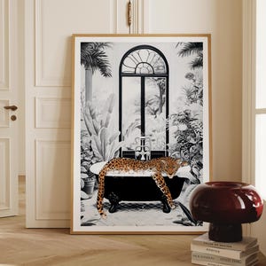 May include: A framed wall art print featuring a black and white illustration of a leopard relaxing in a clawfoot bathtub. The scene includes lush tropical plants and a large arched window in the background, with the leopard in natural colors.