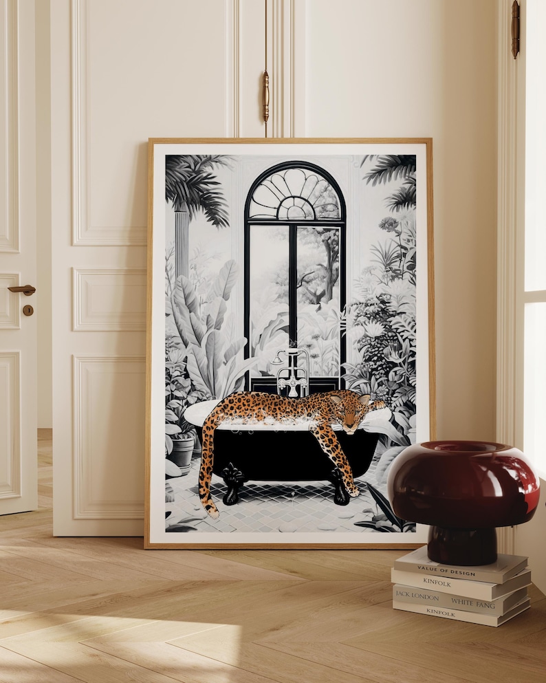 May include: A framed wall art print featuring a black and white illustration of a leopard relaxing in a clawfoot bathtub. The scene includes lush tropical plants and a large arched window in the background, with the leopard in natural colors.