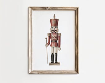May include: A framed print of a traditional nutcracker soldier. The artwork features a red and white uniform, black boots, and a tall hat. The nutcracker holds a staff and stands on a small base. The frame is made of wood.