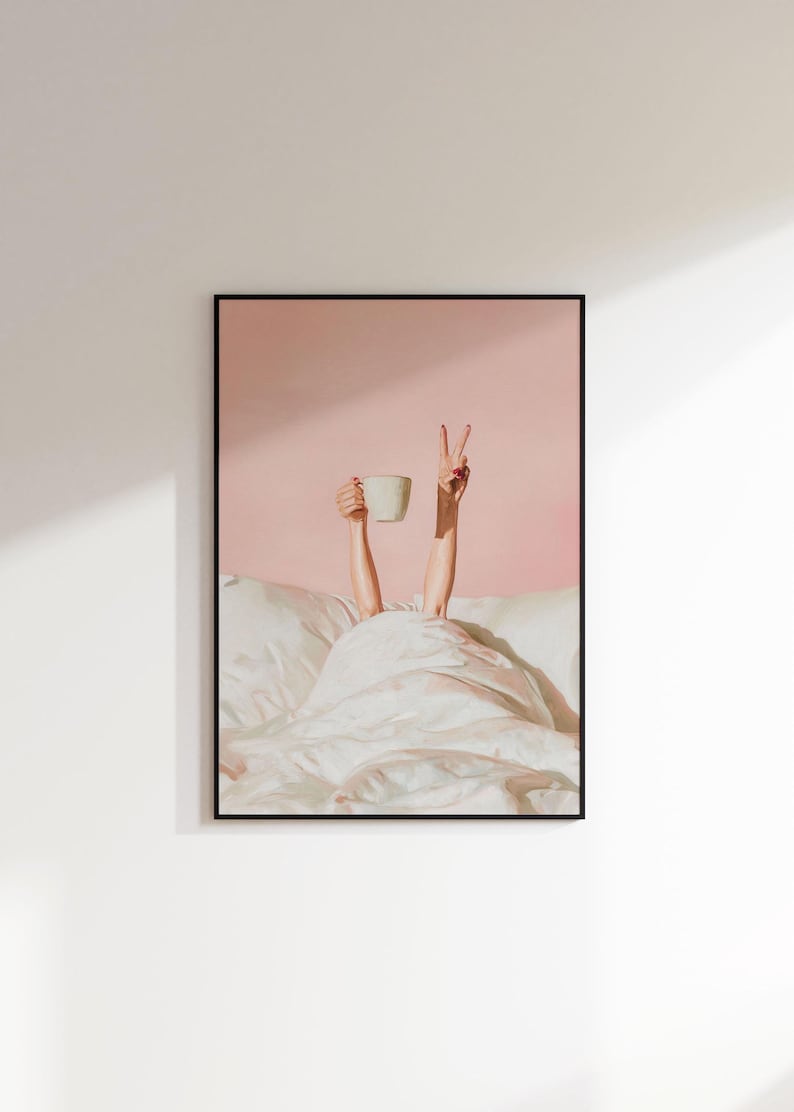 May include: Framed art print featuring a person's arms reaching out from under a white blanket. One hand holds a white mug, the other makes a peace sign. The background is a solid pink color.