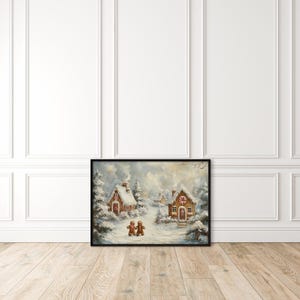 May include: Framed winter landscape art featuring snow-covered gingerbread houses and two gingerbread people. The artwork has a black frame and is set against a white wall and light wood floor. The painting evokes a cozy, festive holiday theme.