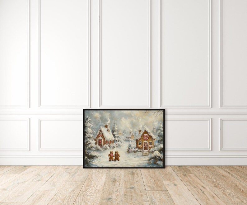 May include: Framed winter landscape art featuring snow-covered gingerbread houses and two gingerbread people. The artwork has a black frame and is set against a white wall and light wood floor. The painting evokes a cozy, festive holiday theme.