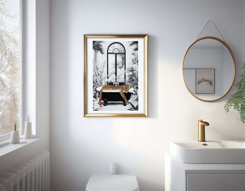 May include: A framed wall art print featuring a black and white illustration of a leopard resting in a clawfoot bathtub. The scene includes tropical plants and an arched window. The artwork is enclosed in a thin, metallic gold-colored frame.