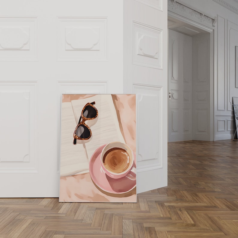 K&ouml;nnte beinhalten: Eine rosa Kaffeetasse mit brauner Fl&uuml;ssigkeit darin, die auf einem rosa Unterteller mit einem wei&szlig;en Notizbuch und einer braunen Sonnenbrille darauf steht. Der Hintergrund ist eine wei&szlig;e Wand.