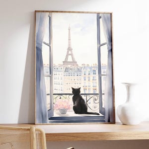 May include: Watercolor print of a black cat gazing out a window at the Eiffel Tower in Paris. The artwork features a framed window with blue curtains, a balcony, and a vase of pink flowers. The print is in a wooden frame.