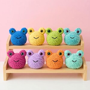Peut inclure: Huit petites peluches grenouilles crochetées et rondes de différentes couleurs : bleu, jaune, vert citron, sarcelle, magenta, lavande, orange et vert menthe. Chaque peluche possède deux yeux en plastique foncé et une bouche noire brodée.