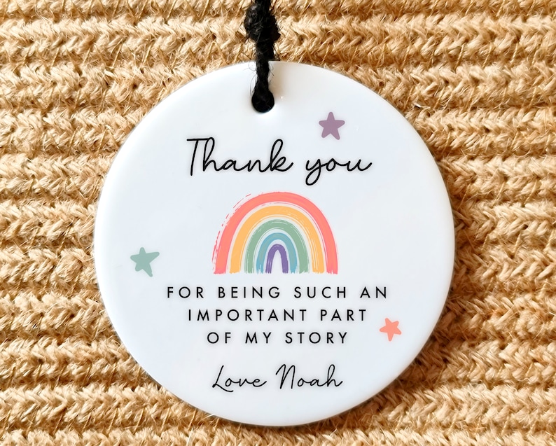 Puede incluir: Adorno de cer&aacute;mica blanca con un arco&iacute;ris y estrellas. El texto dice "Gracias por ser una parte tan importante de mi historia. Con cari&ntilde;o, Noah."