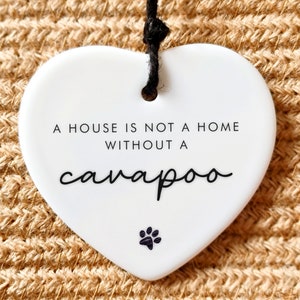May include: White ceramic heart-shaped ornament with black text that reads "A house is not a home without a cavapoo" and a black paw print.