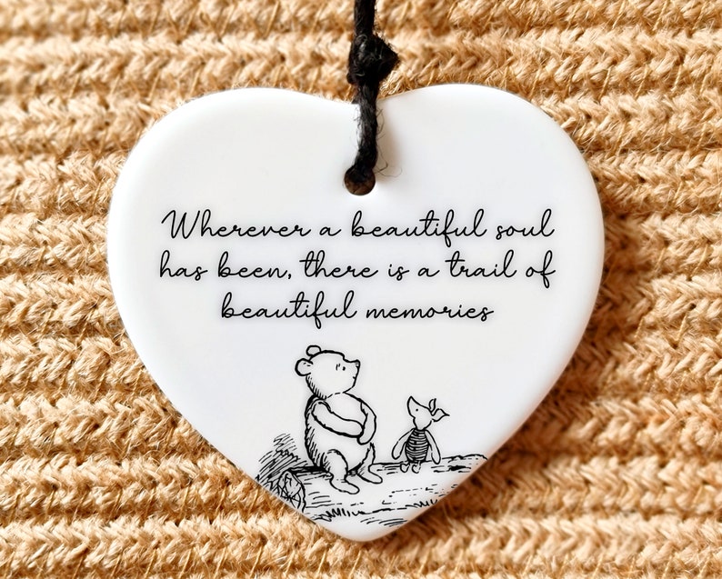 Pu&ograve; includere: Ciondolo a forma di cuore in ceramica bianca con un laccio nero per appenderlo. Il ciondolo presenta un'illustrazione in bianco e nero di Winnie the Pooh e Maialino. Il testo sul ciondolo recita: "Ovunque sia stata un'anima bella, c'&egrave; una scia di bei ricordi."