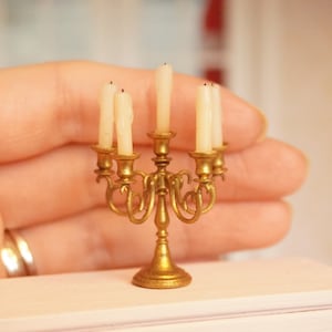 Könnte beinhalten: Goldfarbener Kandelaber mit fünf Kerzenhaltern und fünf weißen Kerzen. Der Kandelaber ist verziert und hat eine dekorative Basis.