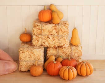 May include: A stack of three miniature hay bales with various sizes and colors of pumpkins and gourds arranged around them.