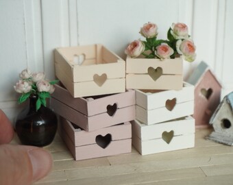 May include: Set of six miniature wooden crates with heart cutouts. The crates are stacked in two groups of three. The crates are painted in shades of cream, pink, and white.