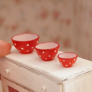 Könnte beinhalten: Drei rote und weiße, gepunktete Rührschüsseln in verschiedenen Größen. Die Schüsseln stehen auf einer weißen, abgenutzten Holzoberfläche.