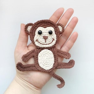 May include: A handmade crochet monkey in shades of brown and cream. The monkey has black button eyes, a smiling face, and outstretched arms and legs. The toy is approximately 6 inches in length.