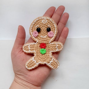 May include: A crocheted gingerbread man ornament with white icing details, black eyes, pink cheeks, and red and green buttons.