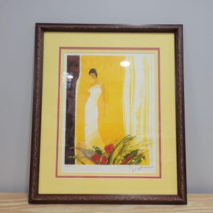 May include: Framed print of a woman in a white dress standing in a yellow room with a window behind her. The print is signed "By Lot" in the bottom right corner.
