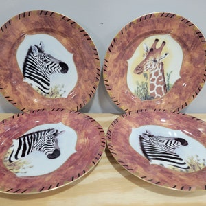 May include: Set of four ceramic dinner plates with a brown and gold rim. Each plate features a different animal: a zebra, a giraffe, a zebra, and a zebra. The animals are depicted in a realistic style against a white background.