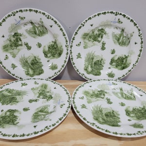 May include: Set of four white ceramic dinner plates with a green ivy border and a green and white rabbit design. The plates feature the text "Peter Rabbit" in blue.