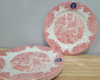 May include: Set of Royal Stafford plates with a red and white design. The plates feature a central illustration of a man in a workshop, surrounded by floral patterns. The plates are a classic design.