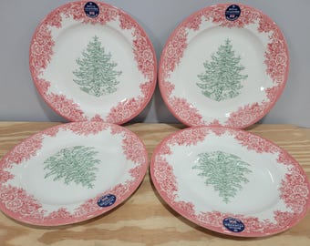 May include: Four white Royal Stafford plates with a pink floral border and a green Christmas tree design in the center. Each plate has a blue and white Royal Stafford sticker. The plates are on a wooden surface.