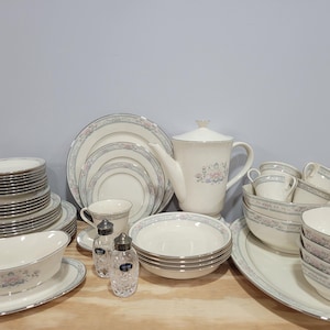 May include: A set of white fine china dinnerware with a floral pattern. The set includes plates, bowls, cups, saucers, a teapot, and serving dishes.