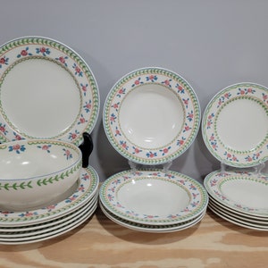 May include: A set of 10 white ceramic plates with a floral design in shades of pink, green, and blue. The plates are arranged in a staggered pattern, with the largest plate in the center and the smallest plates on the edges.