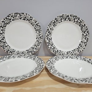 May include: Set of four white ceramic dinner plates with a black floral design. The plates have a scalloped edge.