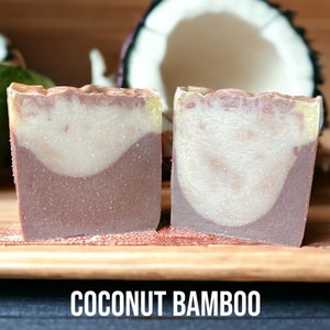 May include: Two bars of handmade soap with a brown, white, and yellow swirl design. The soap is labeled "COCONUT BAMBOO".