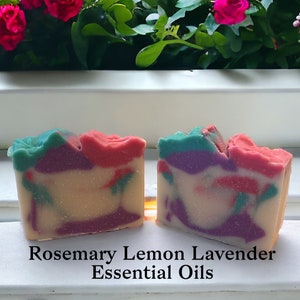 May include: Two bars of handmade soap with a swirl design in shades of pink, purple, and green. The soap is labeled "Rosemary Lemon Lavender Essential Oils".