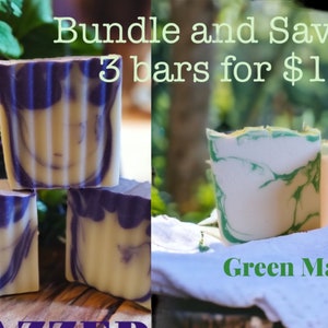 May include: Three bars of handmade soap, two purple and white swirl and one green and white swirl. The soap is arranged in a stack on a wooden surface. The text "Bundle and Save 3 bars for $15" is displayed above the soap. The text "Green Machine" is displayed below the soap.