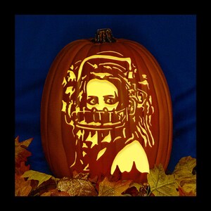 May include: A carved orange pumpkin featuring a glowing yellow silhouette of a person wearing a bear trap over their mouth. The design includes detailed facial features and hair, illuminated from within to create a bright, high-contrast visual effect.