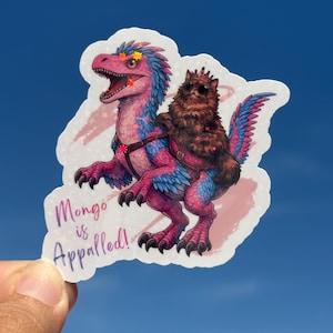 Può includere: Un adesivo raffigurante un dinosauro dei cartoni animati con piume rosa e blu, cavalcato da un gatto marrone con occhiali da sole. L'adesivo ha il testo "Mongo is Appalled!" in un carattere viola.