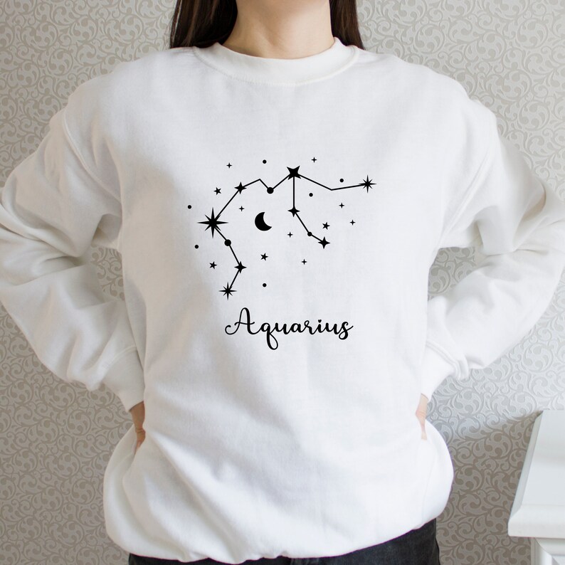 Puede incluir: Sudadera blanca con un gr&aacute;fico negro de la constelaci&oacute;n de Acuario y la palabra "Aquarius" impresa debajo.