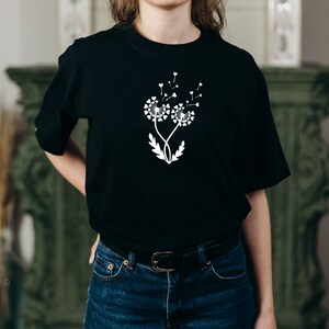 K&ouml;nnte beinhalten: Ein schwarzes T-Shirt mit einem wei&szlig;en Design aus zwei L&ouml;wenzahnpflanzen mit Herzen als Samen. Die L&ouml;wenz&auml;hne werden vom Wind verweht.
