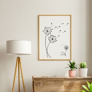 K&ouml;nnte beinhalten: Eine Schwarzwei&szlig;illustration von L&ouml;wenzahnpflanzen mit Samen, die im Wind fliegen, gerahmt in einem hellen Holzrahmen und an einer wei&szlig;en Wand &uuml;ber einer Kommode aus Holz aufgeh&auml;ngt.