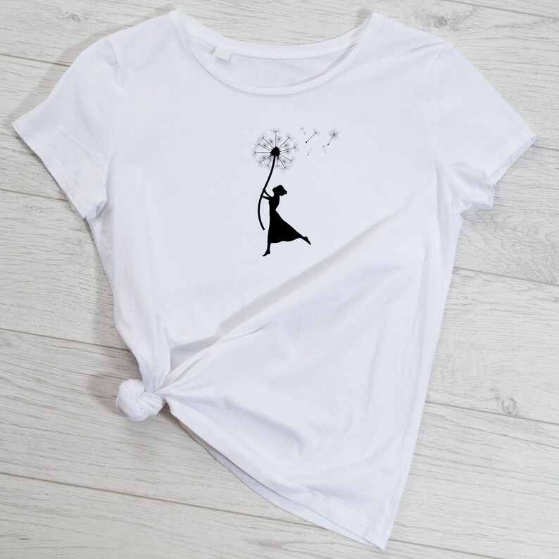 K&ouml;nnte beinhalten: Wei&szlig;es T-Shirt mit einer schwarzen Silhouette einer Person, die einen L&ouml;wenzahn mit Samen h&auml;lt, die im Wind fliegen.