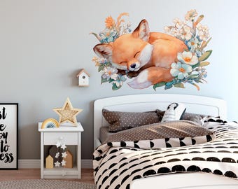 May include: A watercolor wall decal of a sleeping fox surrounded by flowers in shades of orange, white, and blue. The fox is curled up, eyes closed, creating a serene and whimsical scene. The decal is placed above a white bed.