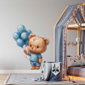 May include: A brown teddy bear wearing a blue shirt and blue shorts holds a bunch of blue balloons. The bear is on a white wall in a nursery with a wooden bed frame and a blue canopy.