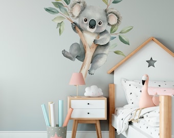 May include: A watercolor koala bear decal on a light blue wall, above a white and wood bed with a pink flamingo toy and a white cloud nightlight on a wooden nightstand.