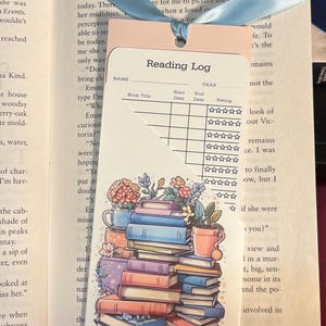 May include: A pink and white reading log bookmark with a stack of colorful books and flowers. The bookmark has a section for the book title, start date, end date, and rating.