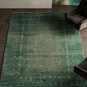 May include: A rectangular, emerald green area rug with a detailed border and central pattern. The rug features a repeating geometric design in a lighter shade of green, creating a textured appearance. The rug is placed on a dark wood floor, with two armchairs visible.
