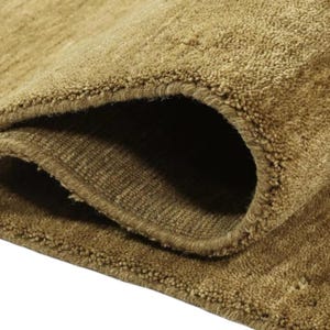 Op de afbeelding: Close-up van een bruin tapijt met een zachte, pluche textuur. Het tapijt is dubbelgevouwen, waardoor de onderkant van de stof zichtbaar is.