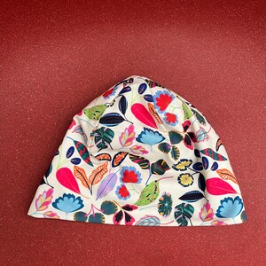 May include: A white beanie hat with a vibrant floral pattern. The design features colorful leaves and flowers in shades of pink, blue, orange, and green. The hat is made of a soft, flexible material.