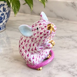 May include: A porcelain mouse figurine featuring a white base with a hand-painted magenta fishnet pattern. The mouse has light blue inner ears, a gold-painted nose, gold-painted paws, and a curved magenta tail resting on a gold-accented base.