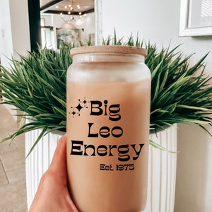May include: A frosted glass jar with a bamboo lid and a straw, filled with a brown liquid. The jar has a black graphic that reads "Big Leo Energy Est. 1975".