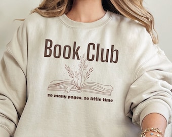 May include: A beige sweatshirt with the text "Book Club" and a graphic of an open book with flowers growing from it. The text below the graphic reads "so many pages, so little time".