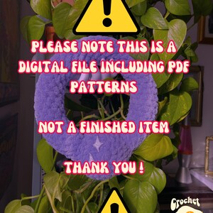 May include: A yellow warning sign with an exclamation point inside. The text reads "Please note this is a digital file including PDF patterns. Not a finished item. Thank you!"  A purple crocheted item is in the background.