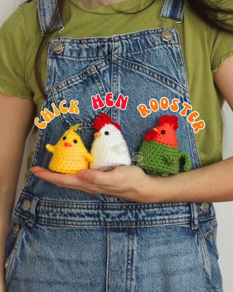 May include: Three crocheted chicken figures: a yellow chick, a white hen, and a green and red rooster. The text "Chick Hen Rooster" is above the figures. The figures are held in a person's hand, against a denim background.