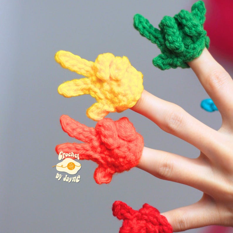 May include: Crocheted finger puppets in yellow, red, and green, each shaped like a hand making a peace sign. The puppets are handmade and feature the text "Crochet by Jayne".